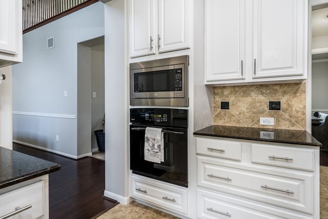 kitchen with black oven, stainless steel microwave, backsplash, white cabinets, and dark stone countertops
