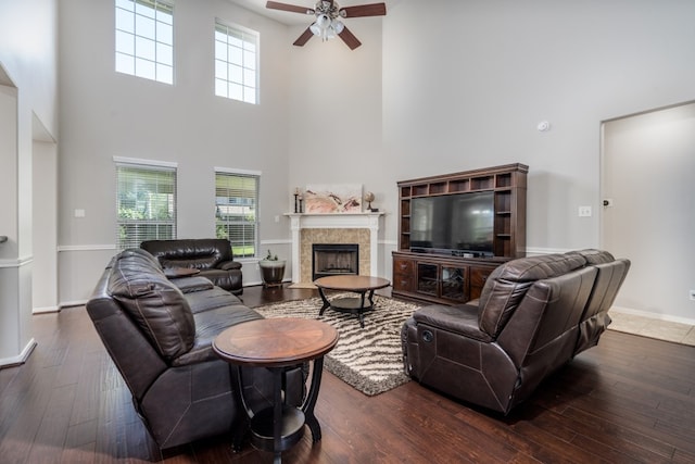 living area with a high ceiling, a ceiling fan, wood-type flooring, a tiled fireplace, and baseboards