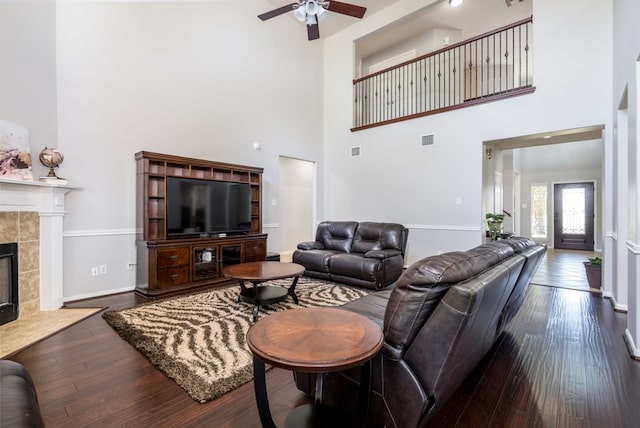 living room featuring a high ceiling, a ceiling fan, hardwood / wood-style floors, a tiled fireplace, and baseboards
