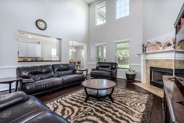 living area featuring wood finished floors, a high ceiling, plenty of natural light, a fireplace, and a chandelier