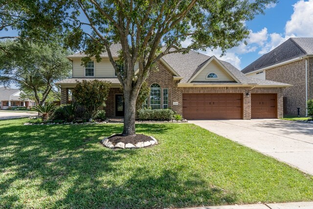 traditional home with brick siding, a garage, concrete driveway, a front lawn, and a shingled roof