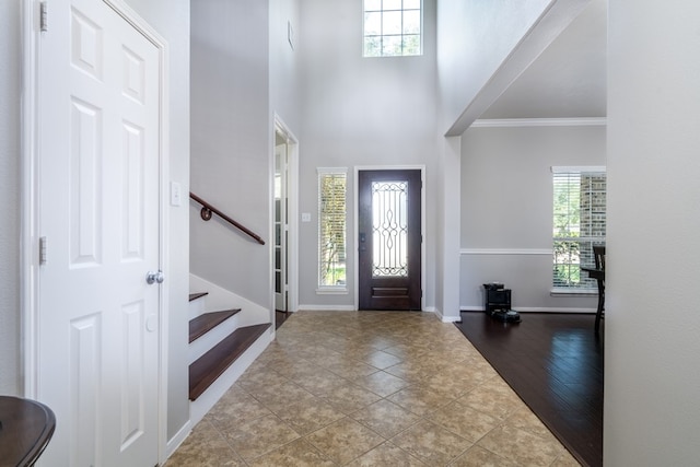 tiled entrance foyer featuring healthy amount of natural light, ornamental molding, baseboards, stairs, and a towering ceiling