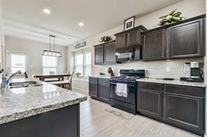kitchen with recessed lighting, black appliances, light stone countertops, decorative light fixtures, and a sink