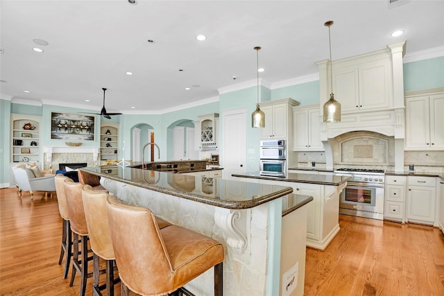 20710 E Sunset Bay Dr, Galveston, TX 77554 - kitchen with light wood-type flooring, stainless steel appliances, a spacious island, ceiling fan, and a fireplace