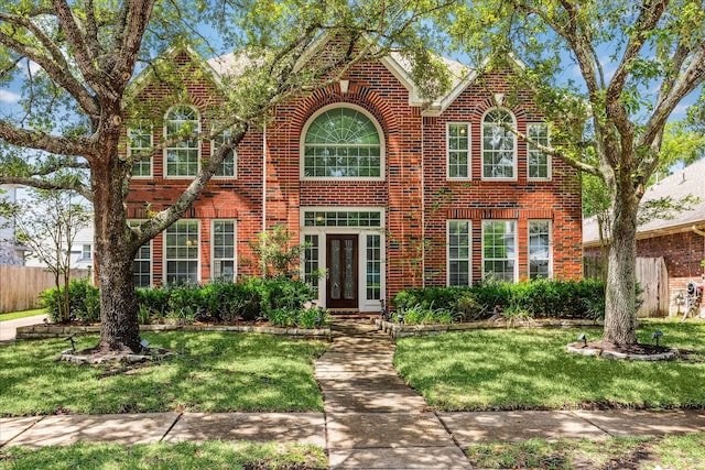 colonial-style house featuring a front lawn, fence, french doors, and brick siding