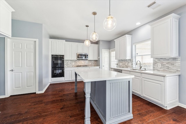 kitchen with stainless steel microwave, light countertops, dobule oven black, a center island, and visible vents