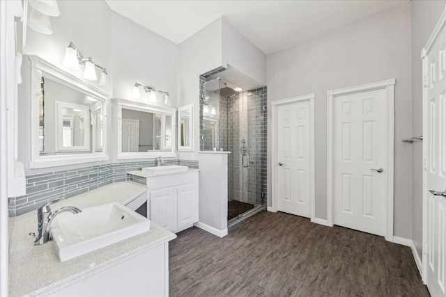 bathroom featuring wood finished floors, decorative backsplash, two vanities, a shower stall, and a sink