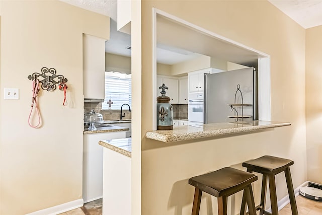18210 Point Lookout Dr, Houston, TX 77058 - kitchen with freestanding refrigerator, oven, decorative backsplash, a sink, and white cabinets
