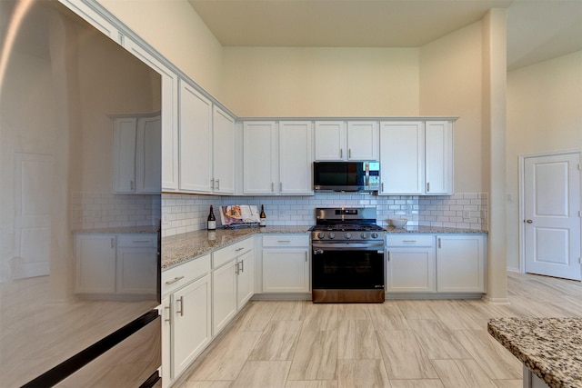 12006 Wooden Mill Ln, Santa Fe, TX 77510 - kitchen with stainless steel appliances, light stone countertops, white cabinetry, and backsplash