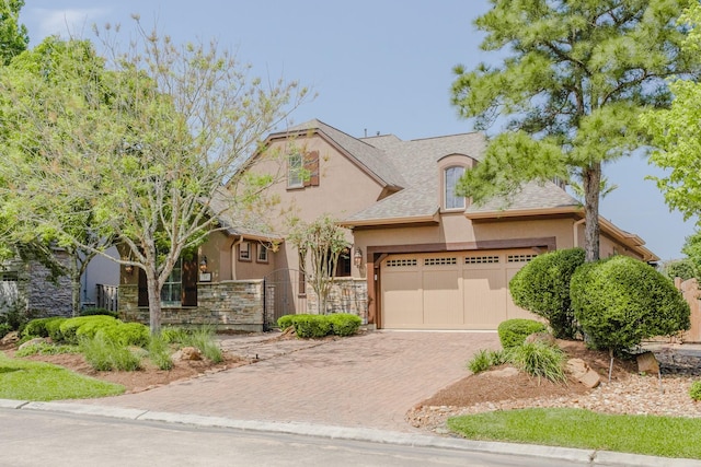 view of front of house featuring stucco siding, decorative driveway, an attached garage, a fenced front yard, and stone siding