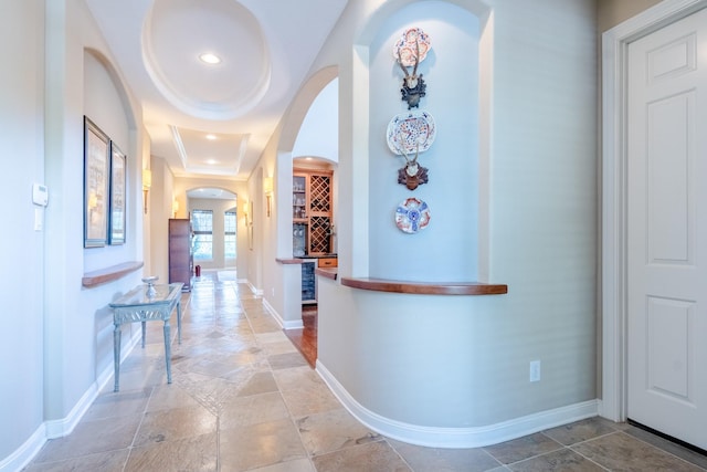 hall featuring arched walkways, baseboards, stone tile floors, and recessed lighting