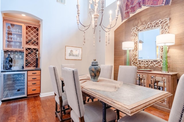 dining space featuring beverage cooler, a dry bar, wood finished floors, arched walkways, and a chandelier