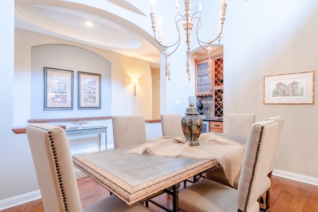 dining space featuring baseboards, wood finished floors, a bar, arched walkways, and recessed lighting