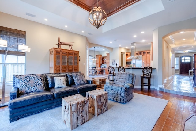 living area with arched walkways, a tray ceiling, recessed lighting, wood finished floors, and baseboards