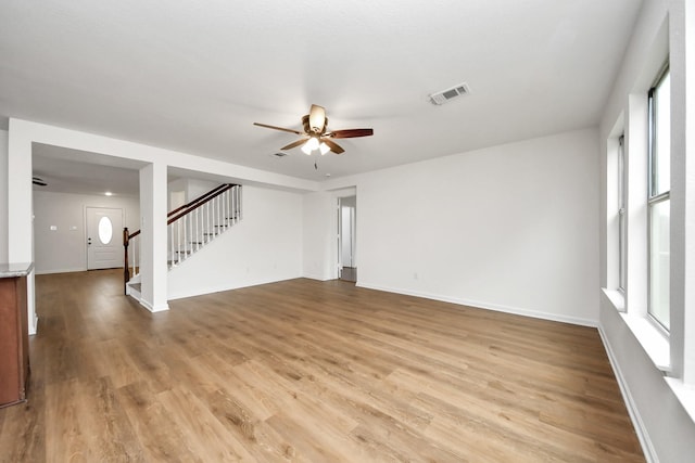 unfurnished living room with light wood-style flooring, visible vents, baseboards, stairs, and a ceiling fan