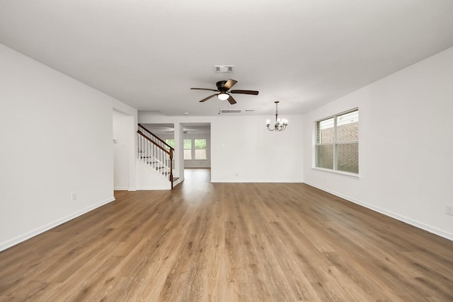 spare room with visible vents, baseboards, wood finished floors, stairway, and ceiling fan with notable chandelier