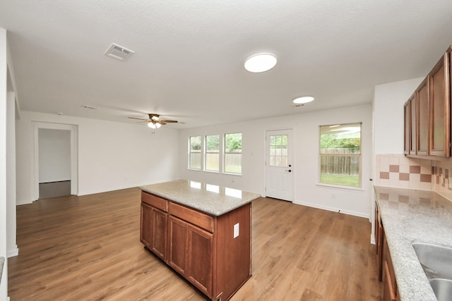 kitchen with open floor plan, brown cabinetry, visible vents, light wood-style floors, and ceiling fan