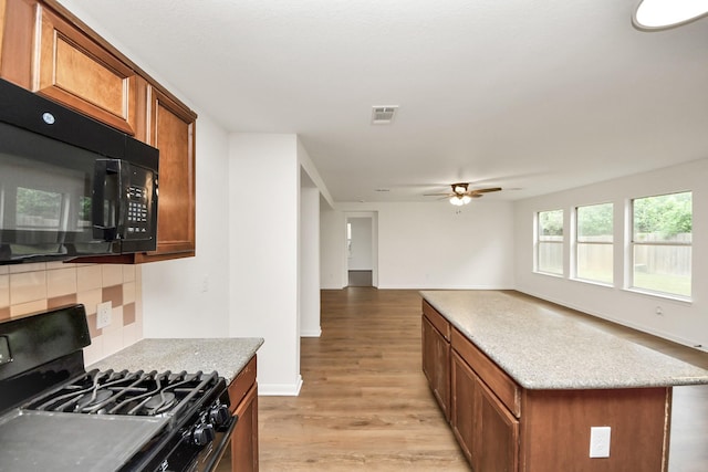 kitchen featuring tasteful backsplash, light wood finished floors, visible vents, black appliances, and brown cabinets