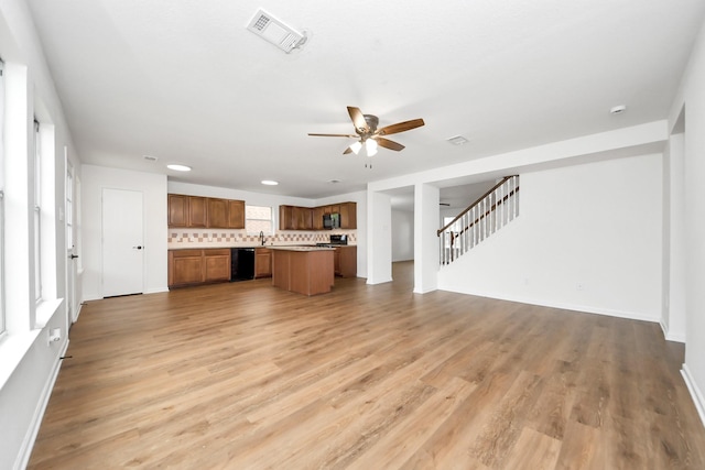 unfurnished living room with a sink, stairway, light wood-type flooring, visible vents, and ceiling fan