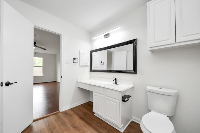 half bath featuring baseboards, wood finished floors, toilet, vanity, and a ceiling fan