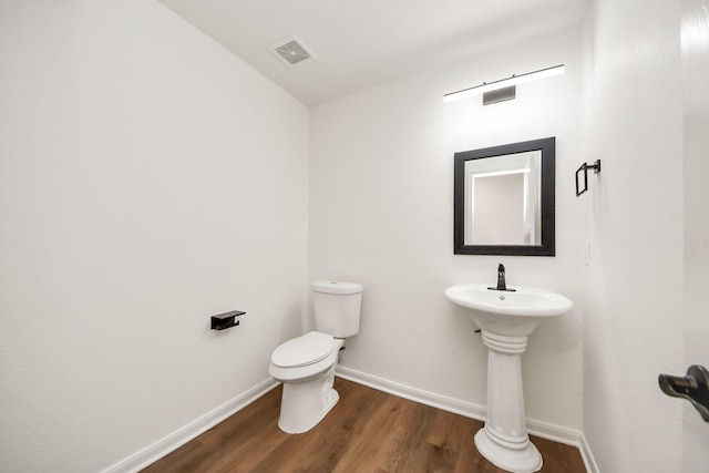 half bath featuring wood finished floors, toilet, baseboards, and visible vents