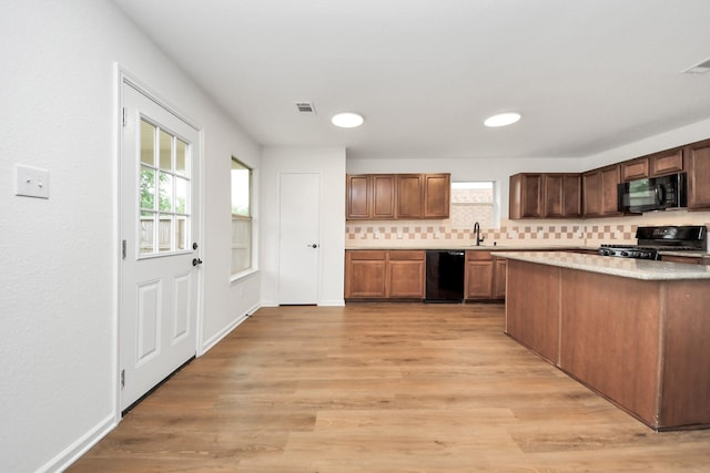 kitchen featuring tasteful backsplash, a sink, light wood finished floors, visible vents, and black appliances