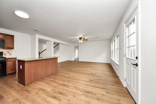 kitchen featuring light wood-style flooring, a center island, backsplash, a ceiling fan, and black appliances
