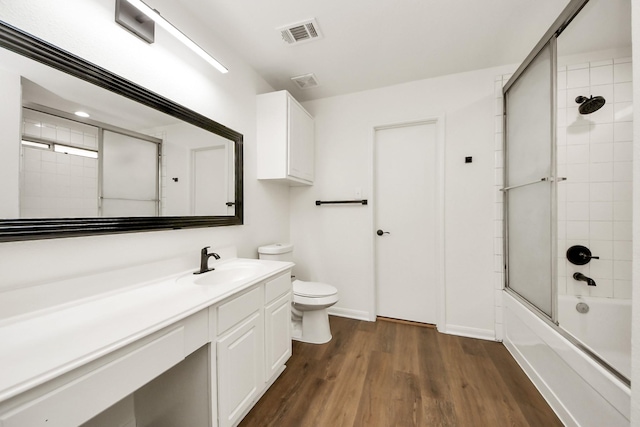 bathroom featuring toilet, vanity, wood finished floors, bath / shower combo with glass door, and visible vents