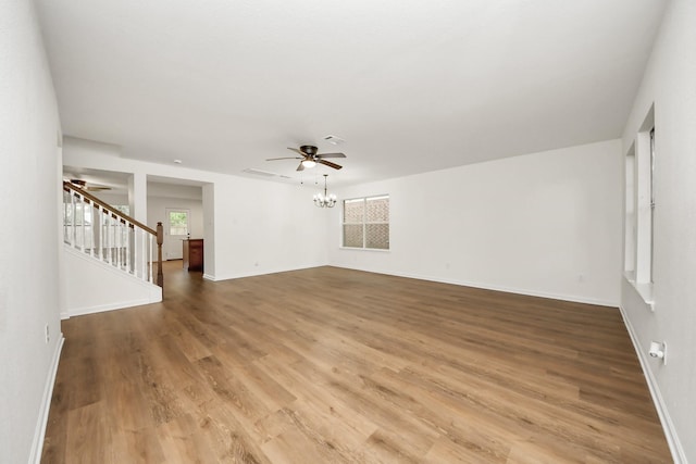 empty room featuring light wood-style flooring, ceiling fan with notable chandelier, stairway, and baseboards