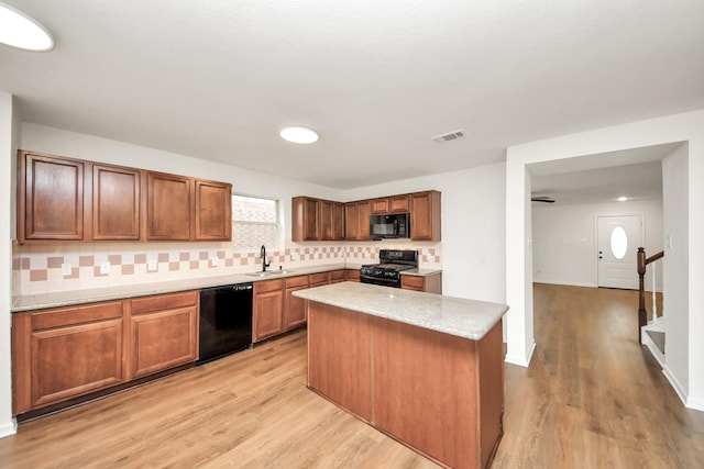 kitchen with a sink, backsplash, black appliances, and light wood-style floors