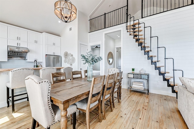 dining room featuring high vaulted ceiling, visible vents, light wood finished floors, stairs, and an inviting chandelier