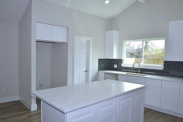 kitchen featuring vaulted ceiling, light stone counters, a sink, and tasteful backsplash