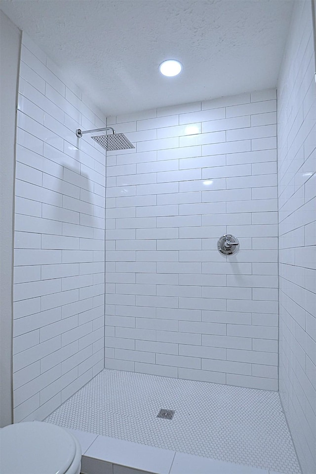 bathroom with a tile shower, toilet, and a textured ceiling