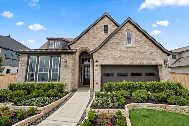 french country home with brick siding, a garage, and fence
