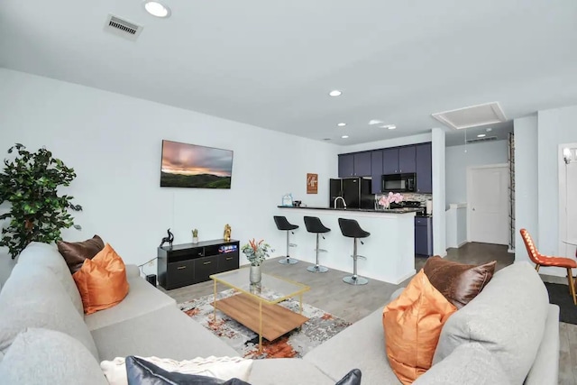 living room with attic access, visible vents, recessed lighting, and light wood-style floors