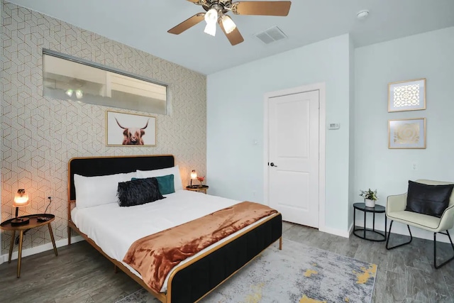 bedroom with wood finished floors, an accent wall, baseboards, visible vents, and a ceiling fan
