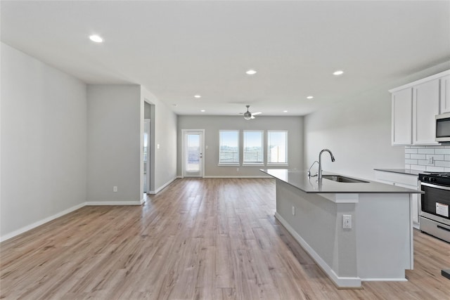 kitchen with open floor plan, a sink, ceiling fan, light wood-style flooring, and appliances with stainless steel finishes
