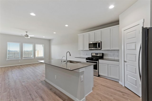 kitchen with decorative backsplash, white cabinets, appliances with stainless steel finishes, a sink, and light wood-type flooring