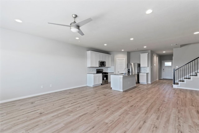 kitchen with open floor plan, light wood-style floors, stainless steel appliances, and tasteful backsplash
