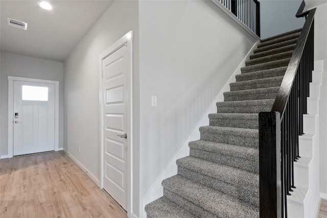 foyer featuring light wood finished floors, baseboards, visible vents, and stairway
