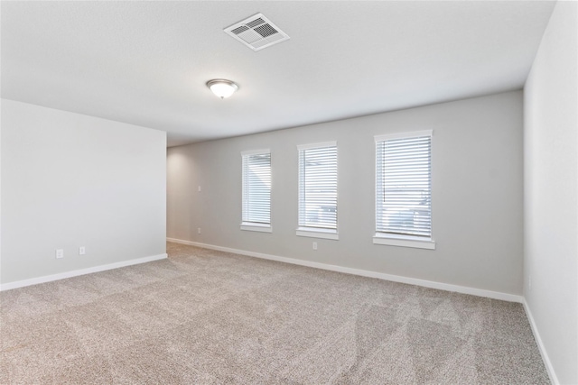 empty room featuring light carpet, a wealth of natural light, visible vents, and baseboards
