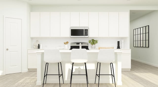 kitchen with white cabinetry, white microwave, a kitchen breakfast bar, and a center island with sink