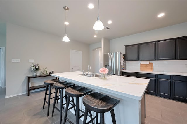 kitchen featuring a sink, an island with sink, stainless steel fridge, arched walkways, and light stone countertops