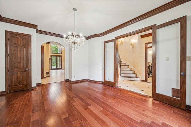 empty room featuring arched walkways, wood finished floors, baseboards, stairway, and a notable chandelier