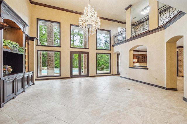 unfurnished living room featuring a high ceiling, a notable chandelier, baseboards, ornamental molding, and arched walkways