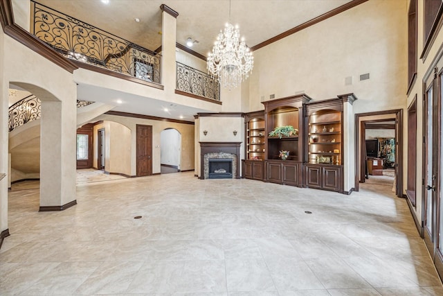 unfurnished living room with a chandelier, a fireplace, ornamental molding, a towering ceiling, and arched walkways