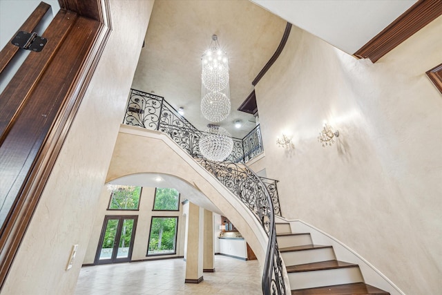 stairway with baseboards, arched walkways, a towering ceiling, french doors, and a notable chandelier