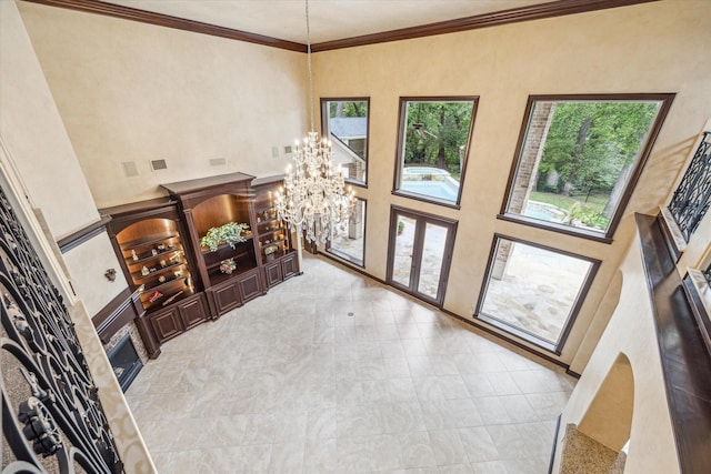 entrance foyer with a chandelier, marble finish floor, a fireplace, crown molding, and a towering ceiling