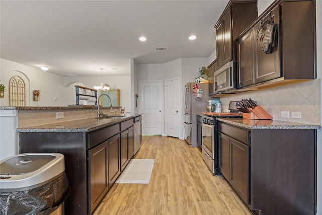 2225 Windy Sail Dr, Texas City, TX 77568 - kitchen featuring light wood-style floors, dark brown cabinetry, dark stone countertops, a sink, and stainless steel appliances