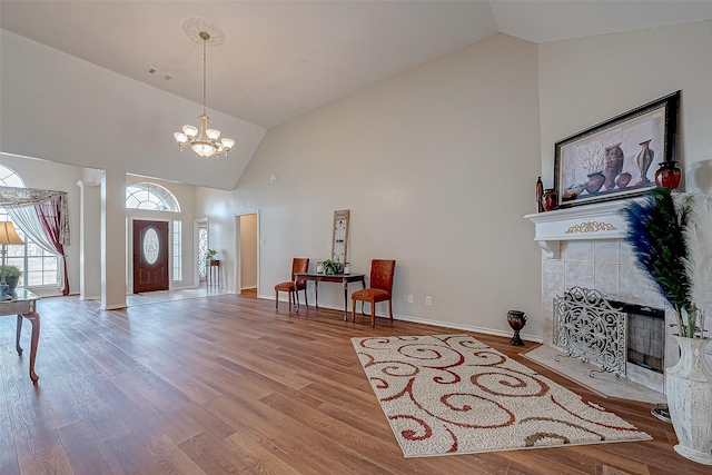 entryway featuring high vaulted ceiling, a tile fireplace, wood finished floors, baseboards, and an inviting chandelier